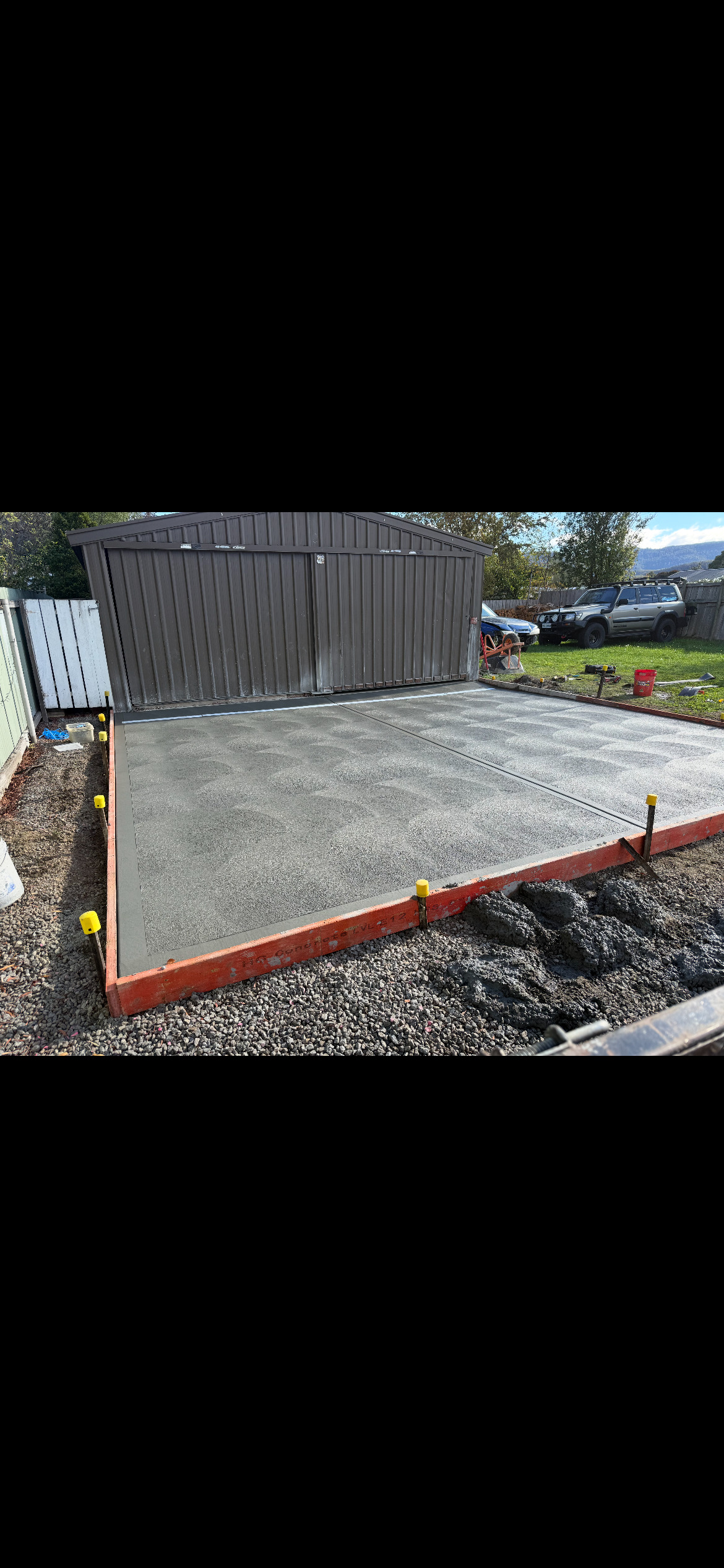 Freshly poured shed slab with orange formwork edges and gravel surround, residential Tasmania